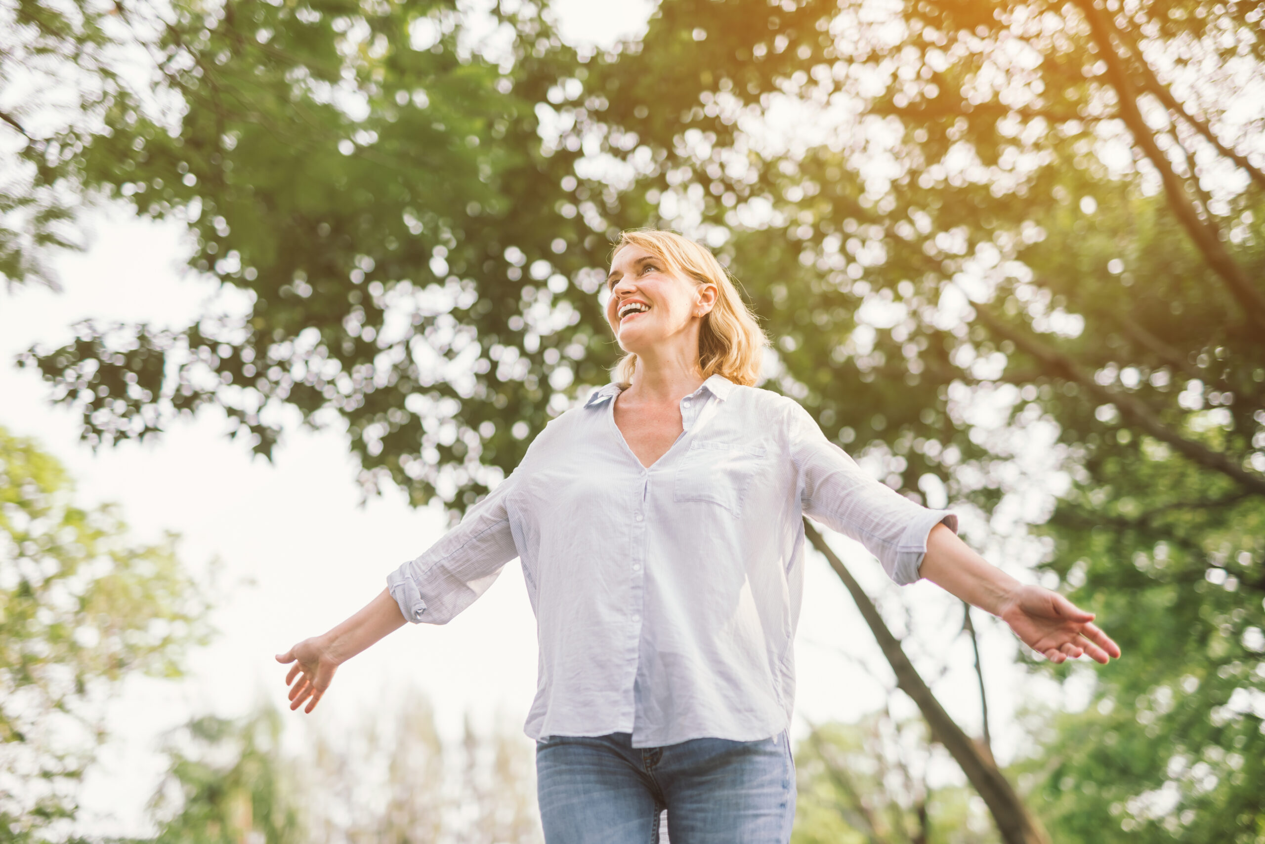 happy woman in spring or summer forest park open arms with happiness, hope and vitality. Caucasian girl relaxing and enjoying life on nature outdoors.